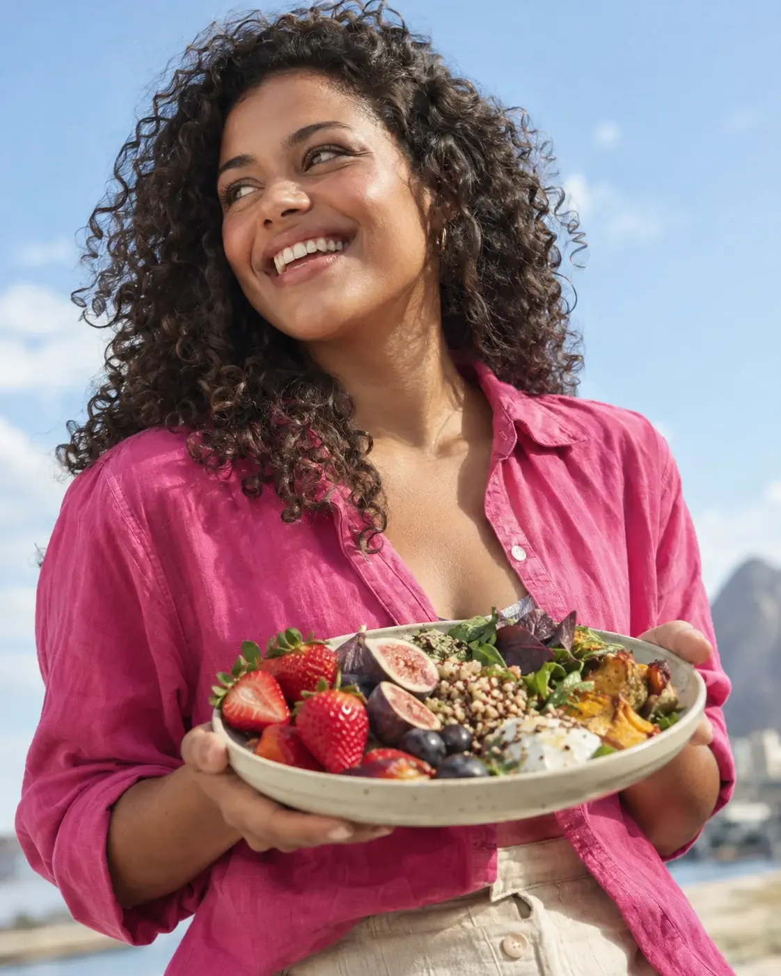 Cena editorial de uma mulher sorrindo com um prato de frutas sob o céu azul